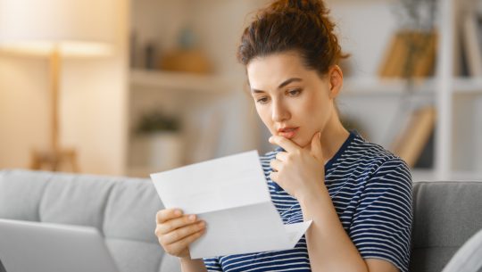 Woman, sitting on the sofa with a paper receipt