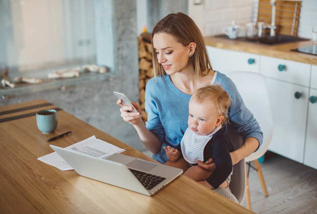 Woman looking at her phone while holding a baby.